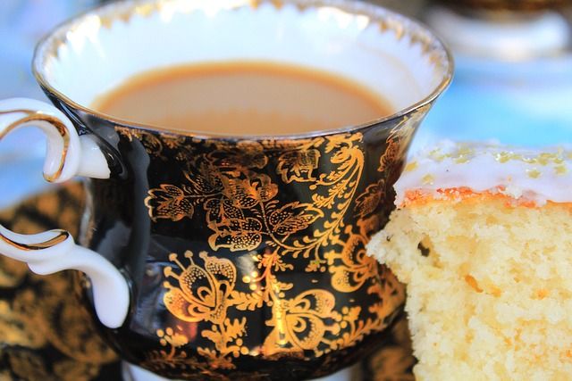Nahaufnahme einer verzierten Teetasse mit Kaffee und einem Stück Kuchen.