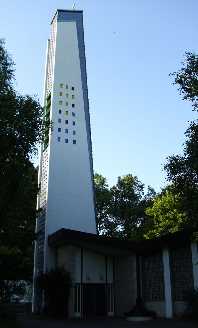 Ein moderner Kirchturm mit bunten Fenstern, umgeben von Bäumen.
