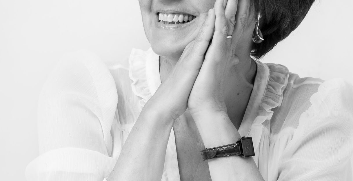 Schwarz-weiß Foto einer lächelnden Frau mit kurzen Haaren, die ihre Hände an die Wangen legt.