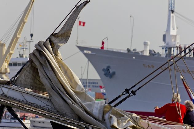 Segelboot mit gefalteten Segeln im Vordergrund, Frachtschiff im Hintergrund im Hamburger Hafen.