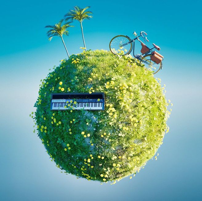 Kleine grüne Kugel mit Blumen, darauf ein Keyboard, ein Fahrrad und zwei Palmen vor blauem Himmel.