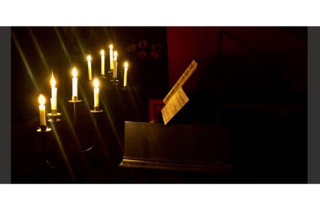 Kerzen auf einem Leuchter beleuchten ein aufgeschlagenes Notenblatt in einem dunklen Raum.