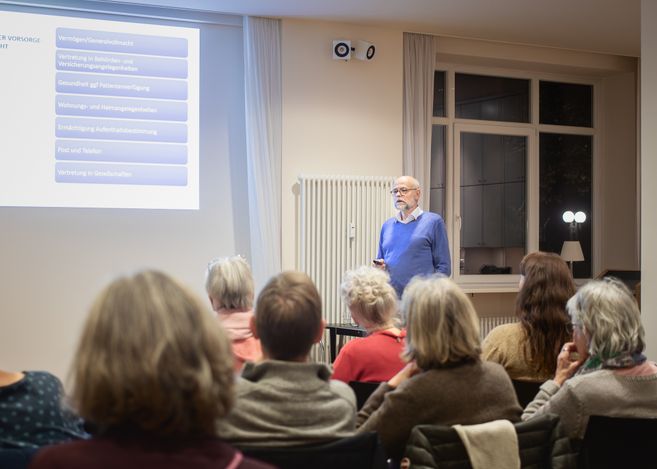 Rechtsanwalt Klaus Jakobsmeyer steht im Hamburg Leuchtfeuer Lotsenhaus vor einer Leinwand. Er spricht zu den Besuchenden der Veranstaltung "Vorsorge und Testament".