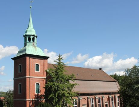 Kirche St. Pankratius in Ochsenwerder mit rotem Backsteinturm und grünem Dach vor blauem Himmel.