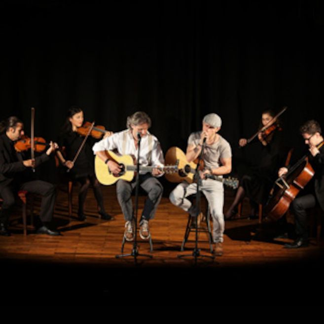 Zwei Musiker mit Gitarren und ein klassisches Streichquartett auf einer Bühne.