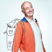 Ein lächelnder Mann in einem orangefarbenen Jackett mit einer gezeichneten Schultasche im Hintergrund.