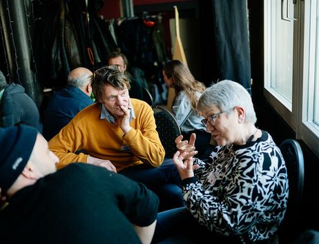 drei Menschen sitzen ins Gespräch vertieft im Kreis und hören einander zu, während eine Person spricht