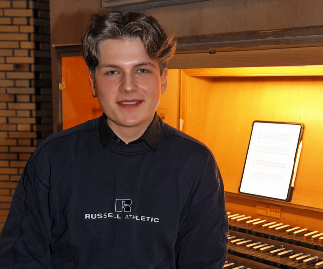 Ein junger Mann sitzt vor einer Orgel mit Notenblatt im Hintergrund.