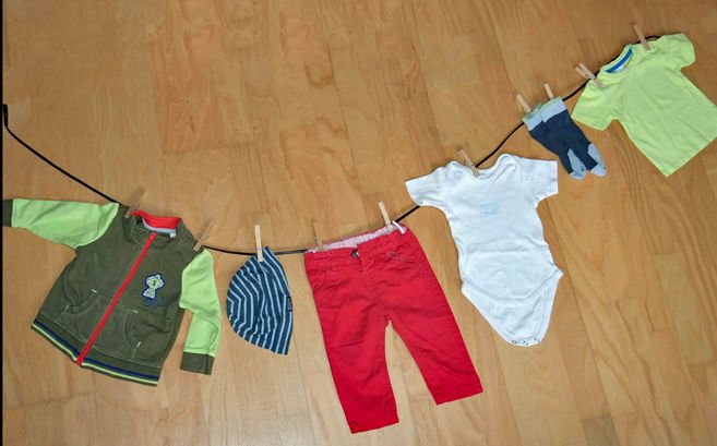 Kinderkleidung hängt an einer Wäscheleine auf einem Holzboden.