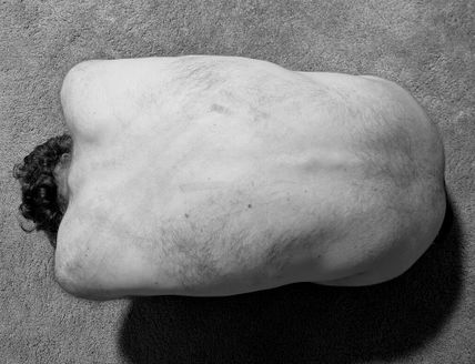 Schwarz-Weiß-Foto eines nackten Rückens einer Person, die auf einem Teppichboden liegt.