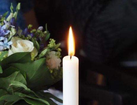 Eine brennende weiße Kerze neben einem Blumenstrauß mit weißen und lila Blüten.