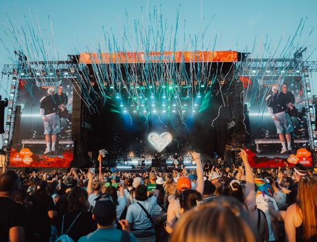 Menschenmenge vor einer großen Festivalbühne mit Lichteffekten und Konfetti.