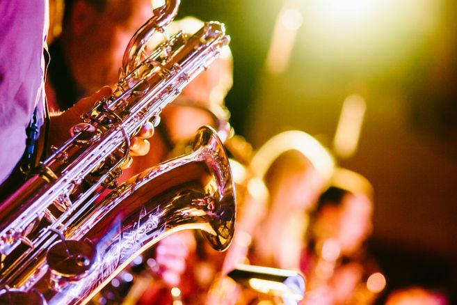 Nahaufnahme eines Saxophons, das von einer Person in einem Konzert gespielt wird, mit verschwommenem Hintergrund und warmem Licht.