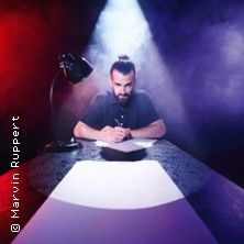 Ein Mann sitzt an einem Tisch und schreibt, umgeben von dramatischer Beleuchtung in Rot und Blau.