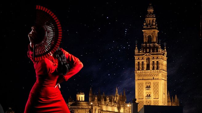 Eine Frau in rotem Kleid mit Fächer vor der Giralda in Sevilla bei Nacht.