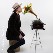 Person mit Hut kniet vor einem Grammophon mit Blumen.
