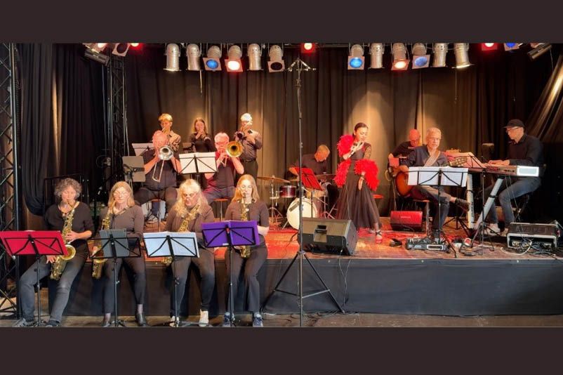 Eine Big Band spielt auf einer Bühne, eine Sängerin in rotem Kleid steht in der Mitte.