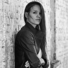 Schwarz-weiß Foto einer Frau in Lederjacke an einer Backsteinwand.