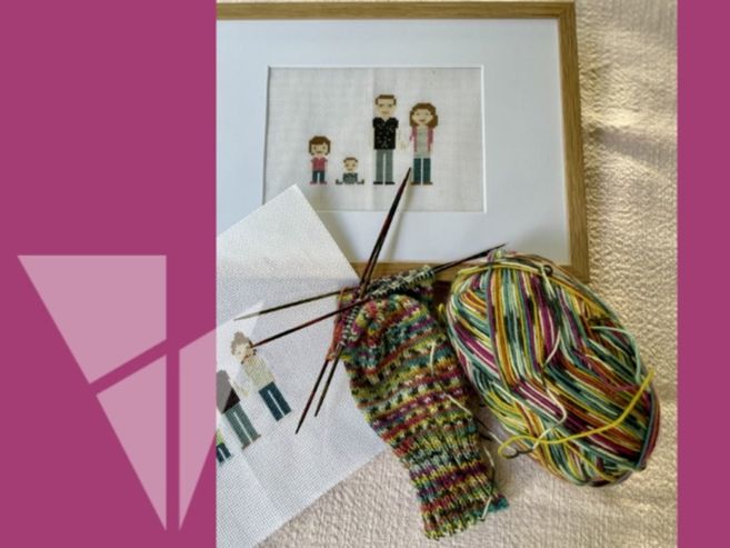 Ein Stickbild einer Familie in einem Rahmen, daneben ein unfertiges Strickprojekt mit buntem Garn und Stricknadeln.