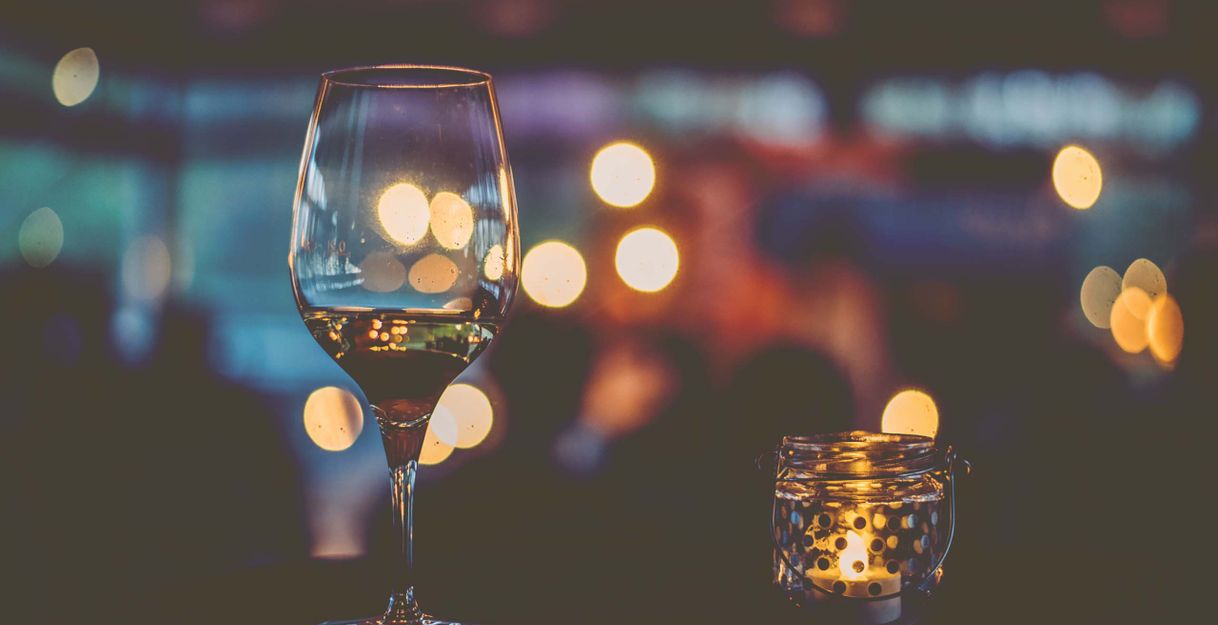 Ein Weinglas und ein Teelicht vor unscharfen Lichtern im Hintergrund.
