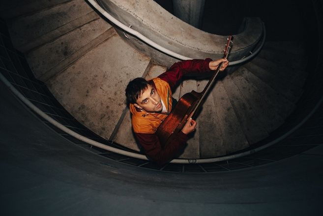 Ein Mann mit Gitarre steht auf einer Wendeltreppe und blickt nach oben.