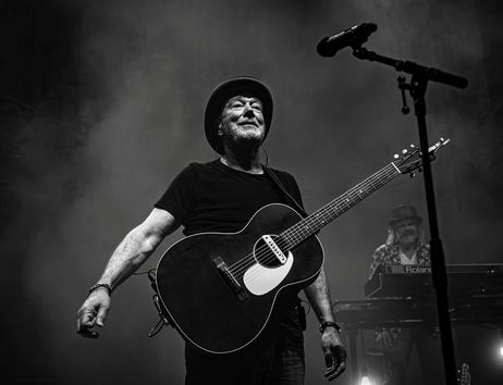Ein Musiker mit Gitarre und Hut auf einer Bühne, im Hintergrund ein Keyboardspieler.