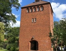 Backsteinturm in einem grünen Garten unter blauem Himmel.