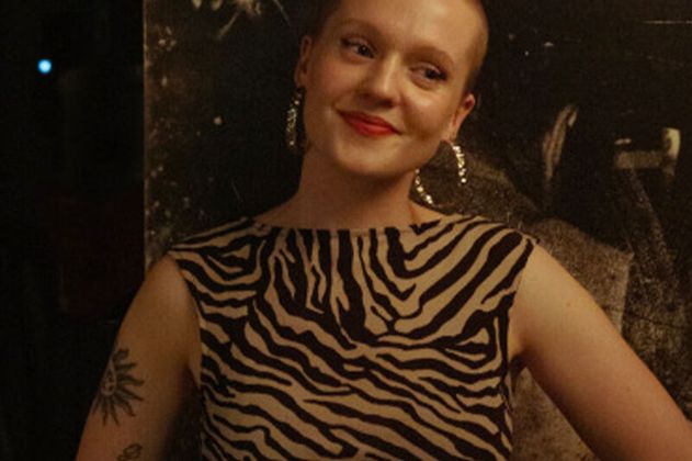Person mit kurzem Haar und Zebra-Muster-Kleid lächelt vor dunklem Hintergrund.