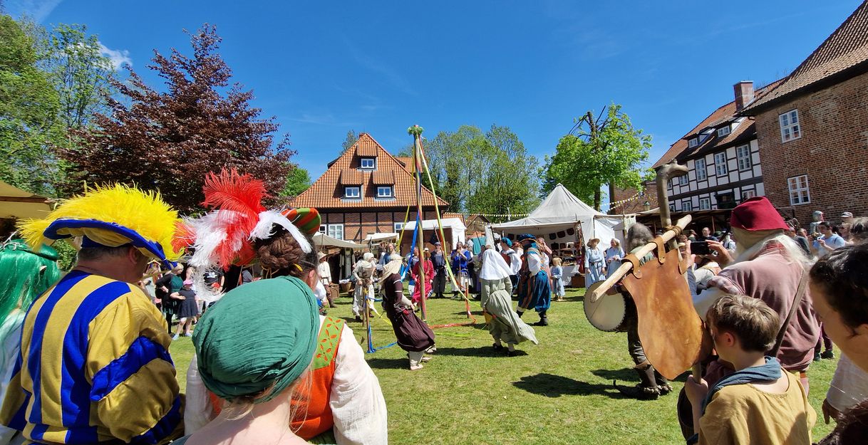 Menschen in historischen Kostümen tanzen um einen Maibaum bei einem Mittelalterfest.