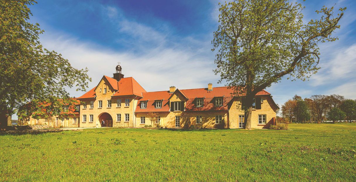 Ein großes, historisches Gebäude mit rotem Ziegeldach auf einem weitläufigen grünen Feld unter blauem Himmel.