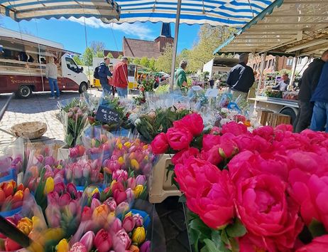 Blumenstand auf einem Wochenmarkt mit bunten Blumensträußen unter einem gestreiften Sonnenschirm.