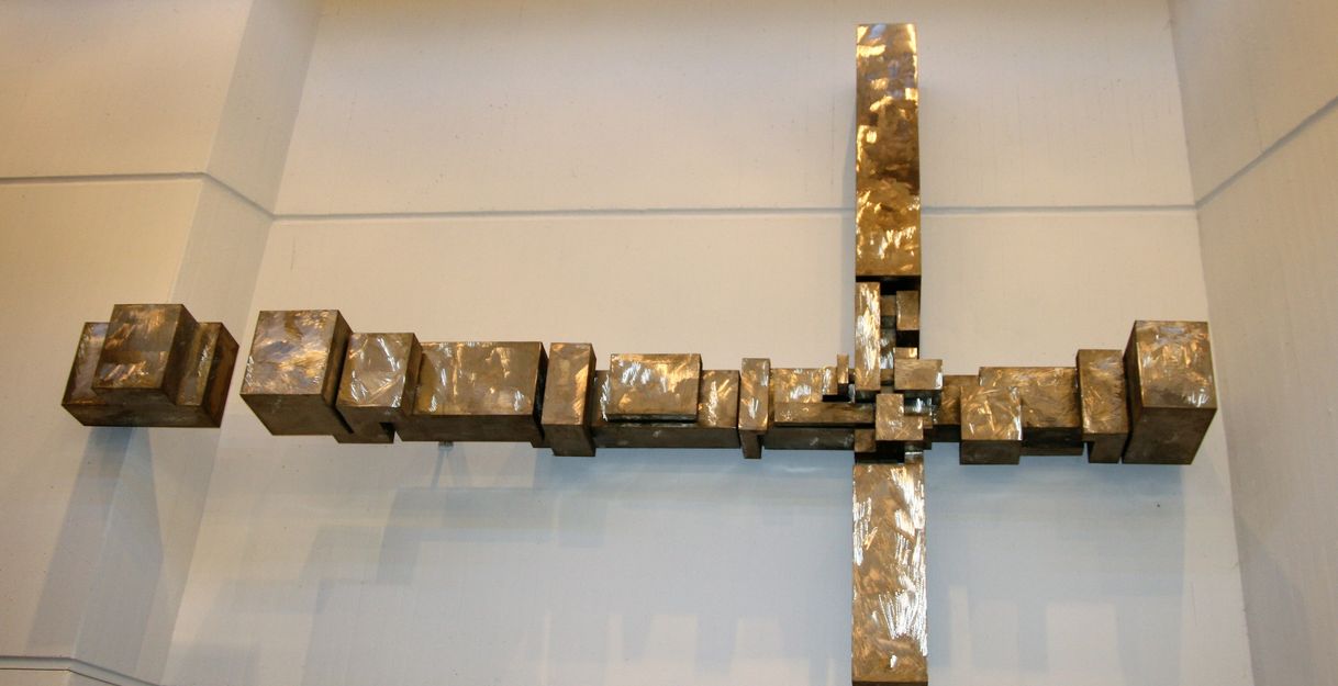 Metallkreuz aus rechteckigen Blöcken an einer Wand.