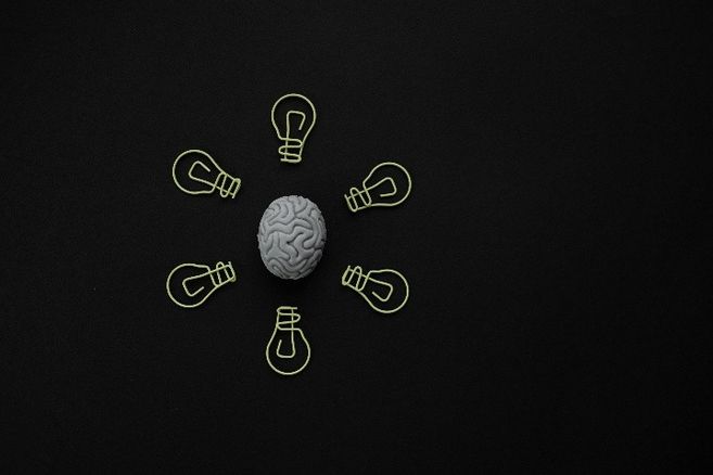 Ein Modell eines Gehirns, umgeben von sechs Glühbirnen-Symbolen auf schwarzem Hintergrund.