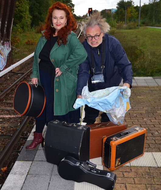 Zwei Personen stehen auf einem Bahnsteig mit mehreren Koffern und einer Karte.