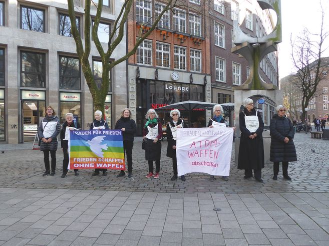 Frauen in Schwarz bei einer Mahnwache mit Bannern gegen Atomwaffen auf einem Platz.