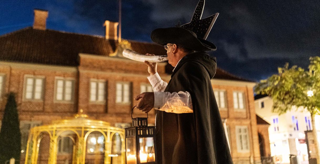 Ein Nachtwächter in historischer Kleidung bläst ein Horn und hält eine Laterne in der Hand, während er durch die Straßen von Eutin geht.