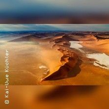 Luftaufnahme einer Wüstenlandschaft mit roten Sanddünen und blauem Himmel.