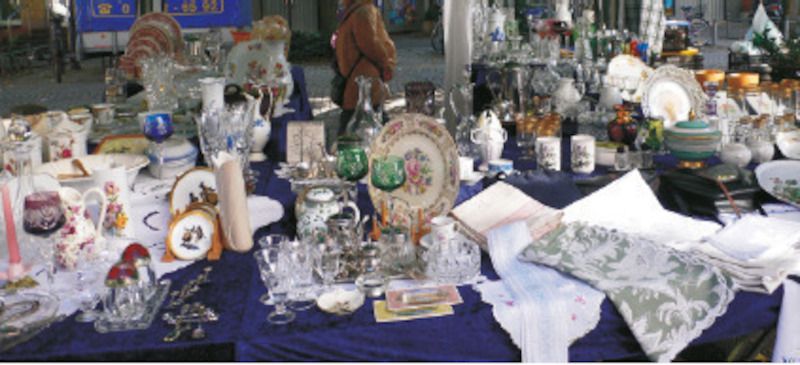 Ein Flohmarktstand mit Geschirr, Gläsern und Textilien auf einem blauen Tuch.