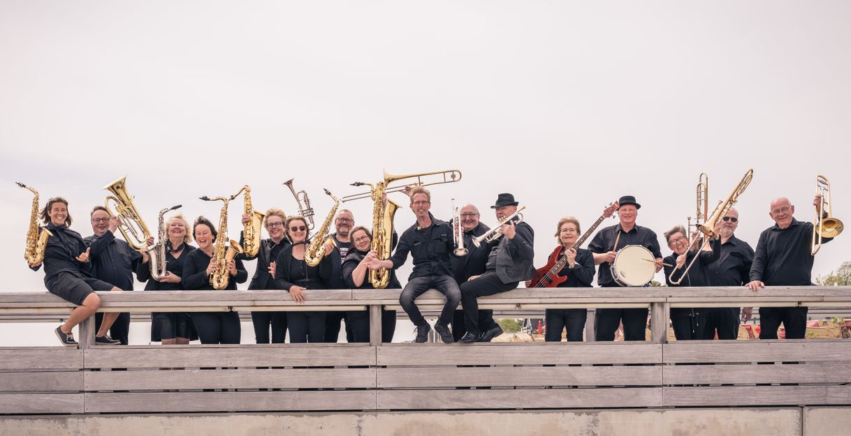 Eine Gruppe von Musikern posiert mit Blasinstrumenten und Schlagzeug auf einer Holzplattform.