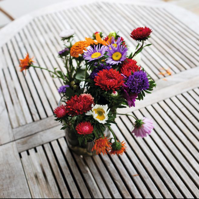 Ein bunter Blumenstrauß in einer Vase auf einem Holztisch mit Gittermuster.