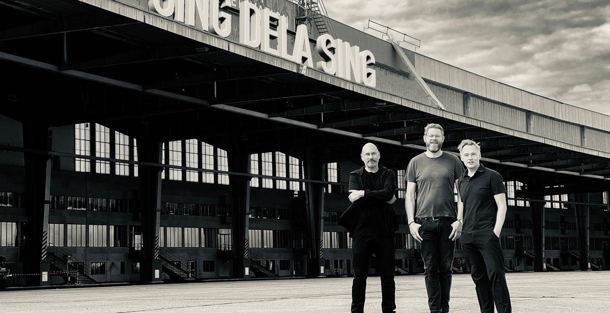 Schwarzweiß Foto. Sing de la Sing stehen vor einem Gebäude auf dem ihr Bandname zu lesen ist.