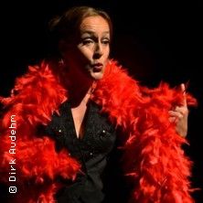 Eine Frau in schwarzem Outfit mit rotem Federboa auf einer Bühne.