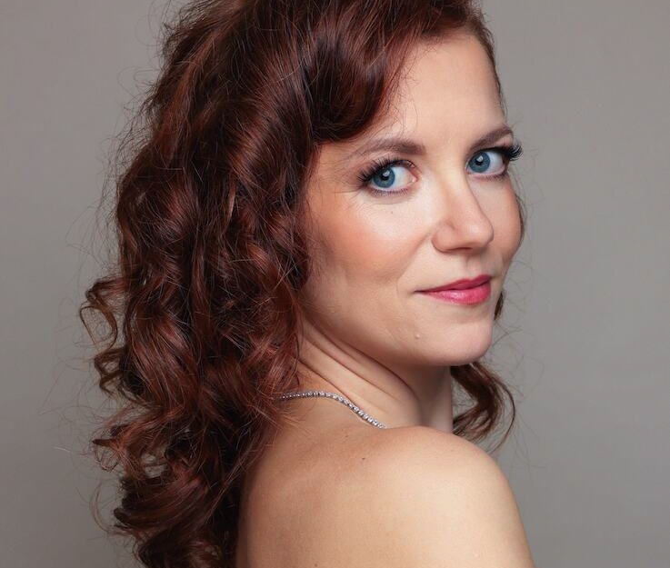 Porträt einer Frau mit lockigem, rotem Haar und blauem Kleid, die über die Schulter schaut.