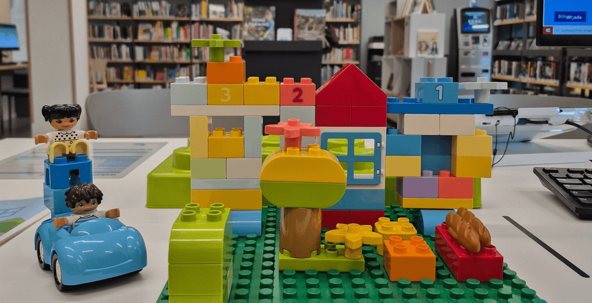 LEGO DUPLO Spielszene in einer Bibliothek mit Figuren und Bauklötzen.