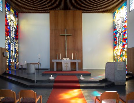 Innenansicht einer Kirche mit Altar, Kreuz und bunten Glasfenstern.