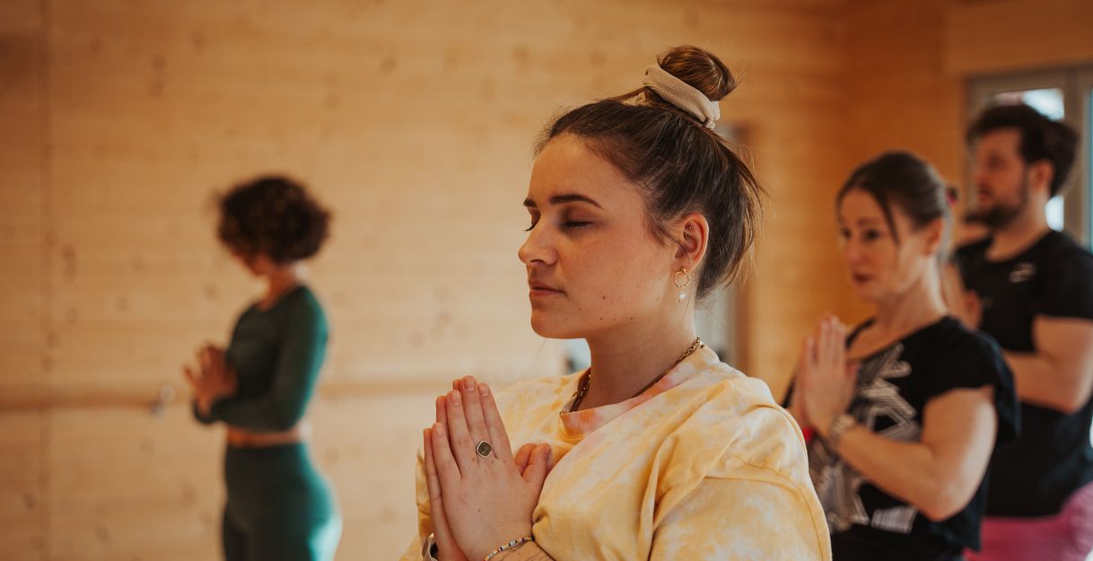 Menschen in einem Yoga-Kurs in einem Raum mit Holzwänden, die meditieren.