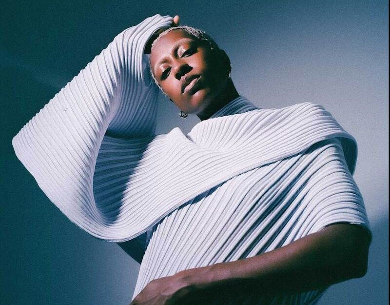 Person in einem strukturierten, weißen Outfit vor einem blauen Hintergrund.