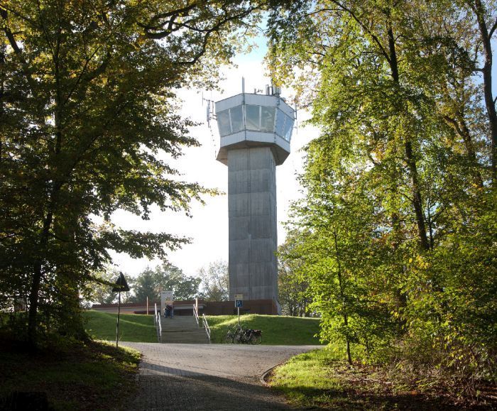 Ein Aussichtsturm in einem Waldgebiet, umgeben von Bäumen und einem Weg, der zum Turm führt.