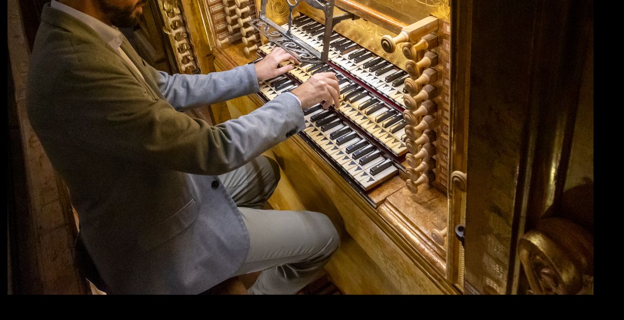 Ein Mann spielt eine historische Orgel mit mehreren Manualen und Registern.