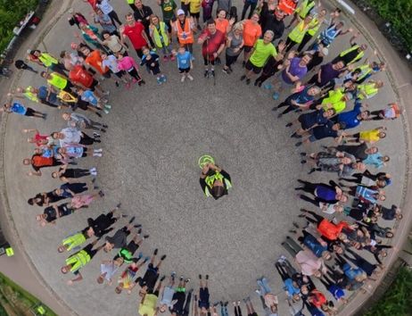 Gruppe von Menschen steht im Kreis auf einem Platz, umgeben von Gebäuden und Bäumen.